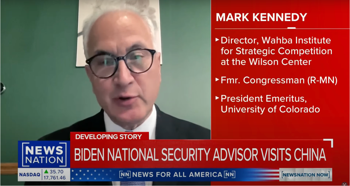 A man in glasses and a suit speaks during a video interview. On-screen text identifies him as Mark Kennedy, listing his titles and affiliations. The news headline reads, Biden National Security Advisor visits China.
