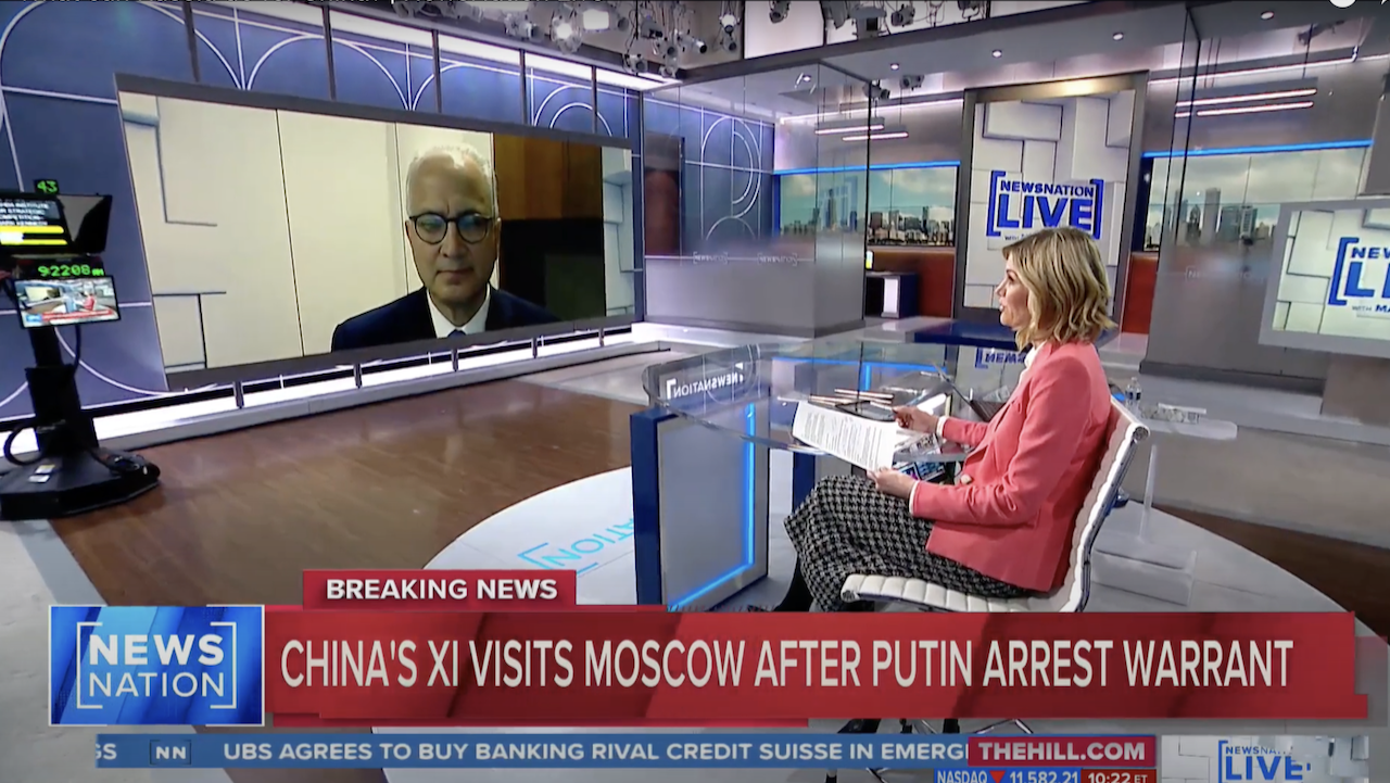 A female news anchor in a pink blazer interviews a man via video call on a large screen in a modern TV studio. The headline reads, Chinas Xi visits Moscow after Putin arrest warrant.