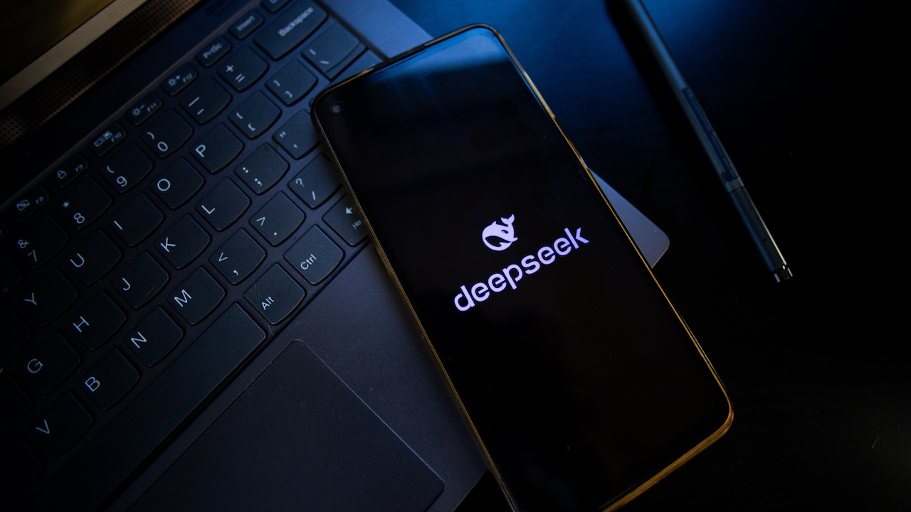 A smartphone displaying the deepseek logo rests on a laptop keyboard, with a stylus pen nearby on a dark surface.