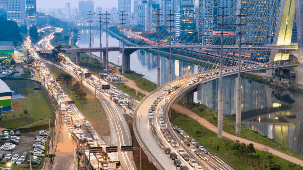 Aerial view of a busy highway with heavy traffic and bridges crossing a river, surrounded by modern high-rise buildings in a city at dusk.