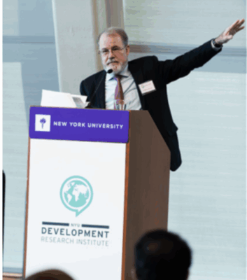 A man speaks at a podium labeled Development Research Institute while gesturing; below, a woman stands at a microphone among a seated audience.
